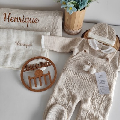 Conjunto de roupa de bebé creme com macacão, gorro, toalhas bordadas e vaso com flores azuis