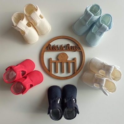 Cinco pares de sapatos tricotados para bebé em várias cores com placa de madeira no centro