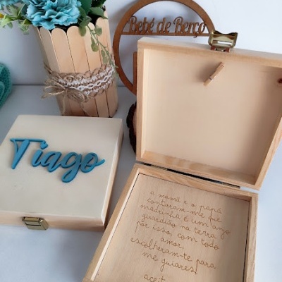 Caixas de madeira com nomes e texto gravado, flores azuis em vaso de madeira e placa redonda decorativa.