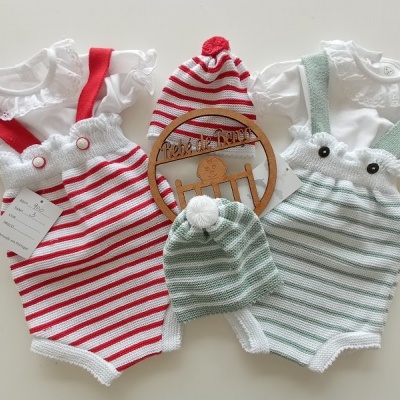 Conjuntos de roupa de bebé com jardineiras às riscas vermelhas e verdes, camisolas brancas com gola rendada e gorros às riscas com pompons