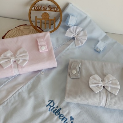 Roupas infantis em azul, rosa e cinza com laços brancos e nome bordado Rúben sobre fundo claro e disco de madeira Bebé de Peso