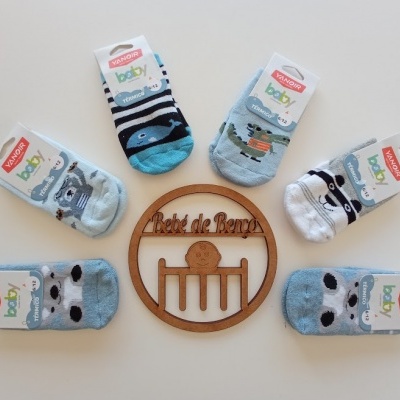 Seis pares de meias para bebé com padrões de animais e riscas, etiquetadas, dispostas em círculo em volta de um emblema de madeira com texto e figura.