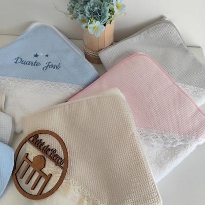 Toalhas infantis em várias cores com bordados e renda junto a um arranjo floral