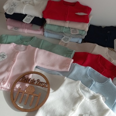Cardigans de bebé de várias cores empilhados com letreiro Petit de Bébé