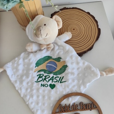 Cobertor de pelúcia branco com ursinho e bordado da bandeira do Brasil.