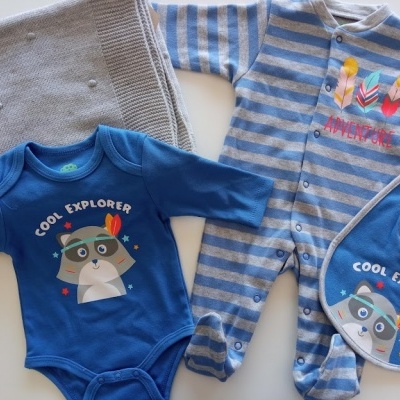Conjunto de bebé azul com personagem COOL EXPLORER e pijama riscado sobre manta cinzenta