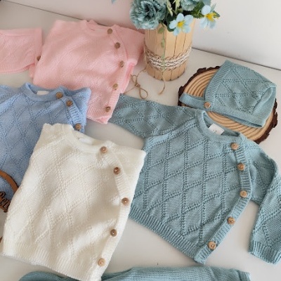 Conjunto de roupa de bebé em malha com botões de madeira e vaso com flores artificiais