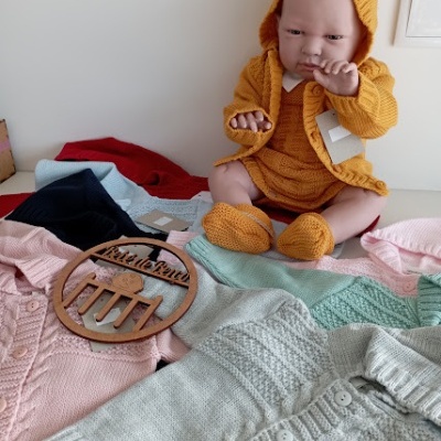 Boneca com roupa de malha mostarda com várias roupas de malha em cores pastel e vermelhas à sua volta