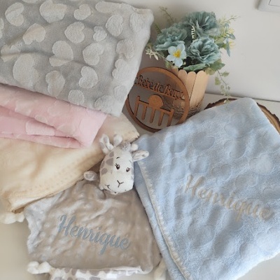 Mantinhas e brinquedo de pelúcia com padrão de corações e nomes bordados