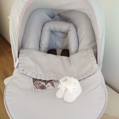 Carrinho de bebé cinzento claro com capota branca e sapatinhos brancos