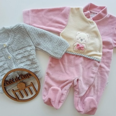 Conjunto de roupa de bebé com malha azul, macacão rosa com bordado de ursinho e placa de madeira com texto