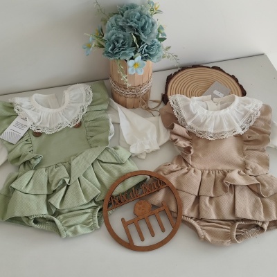 Dois bodies infantis verde e bege com folhos e renda, babete branco, flores artificiais e elementos de madeira