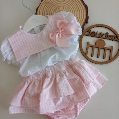 Conjunto infantil branco e rosa com saia e laço, em fundo claro e objeto de madeira