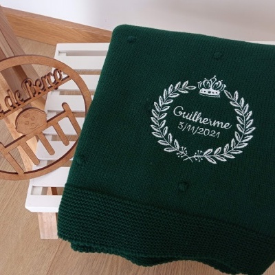 Cobertor verde escuro com bordado branco e cabide de madeira pendurado na cadeira branca