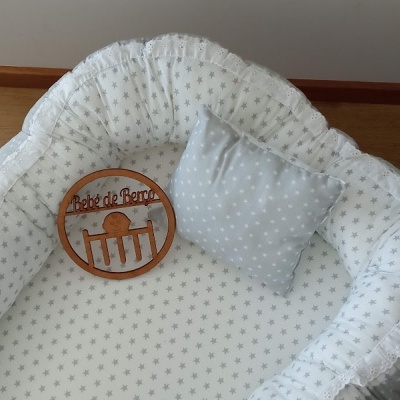Mini berço redondo acolchoado branco com almofada cinzenta e placa de madeira com texto