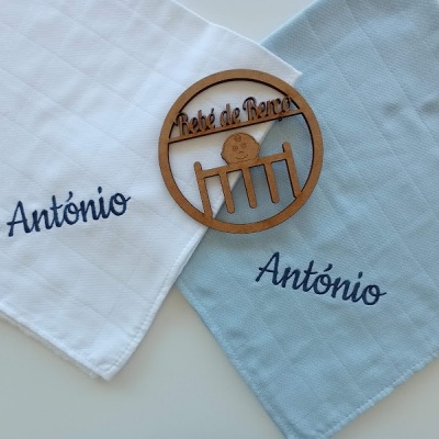 Dois panos de tecido com nome António bordado e um círculo de madeira com texto gravado