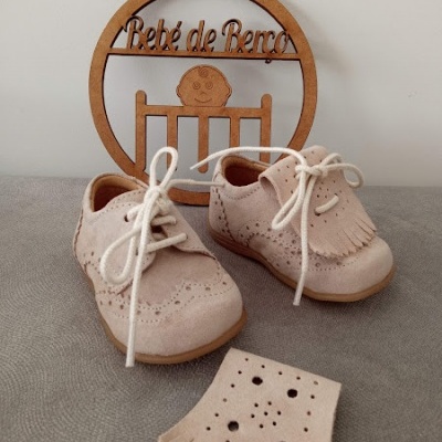 Sapatos de bebé em camurça bege com atacadores brancos e placa decorativa de madeira com texto 
