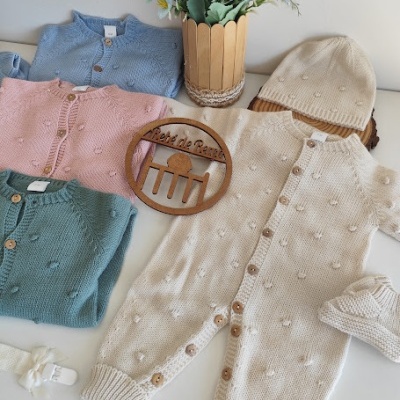 Roupas de bebé coloridas em malha com textura decorativa, vaso com flores e placa decorativa em madeira