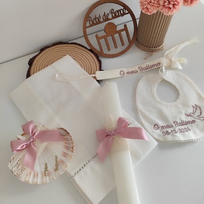 Conjunto para batismo com toalha, vela, concha, babete bordada, marcador e vaso com flores.