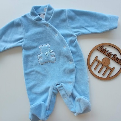 Macacão azul para bebé com ursinho bordado e fecho de botões ao lado de placa de madeira