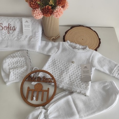 Conjunto de roupa de bebé branca em malha, toalha bordada, vaso com flores e decoração de madeira