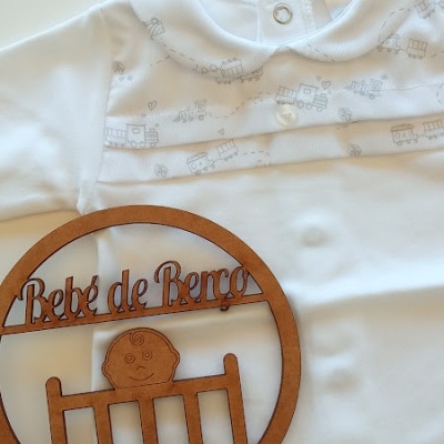 Macacão branco para bebé com padrão de comboios cinza e decoração em madeira com texto 'Bebé de Berço'.