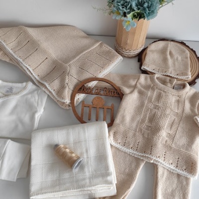 Roupas de bebé em malha bege com detalhes brancos e acessórios em fundo branco