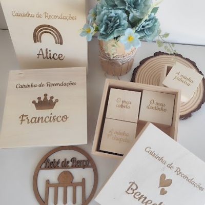 Caixinhas de recordações personalizadas em madeira com nomes gravados e pequenos blocos para guardar memórias, decoradas com flores artificiais azuis e brancas.