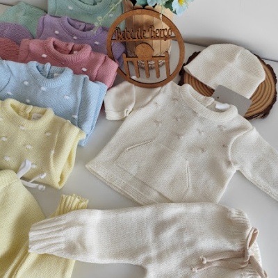 Conjunto de roupa de bebê branca em malha com outras roupas coloridas ao redor e flores azuis