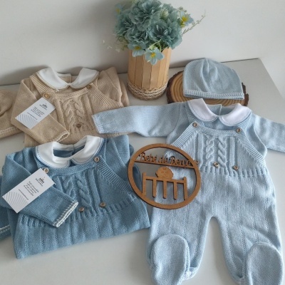 Conjunto de roupas de bebé em malha azul e bege com gola branca e botões, chapéu azul e flores artificiais