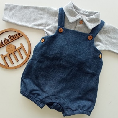 Conjunto de roupa de bebé com camisola cinzenta e macacão azul escuro, e placa redonda decorativa em madeira