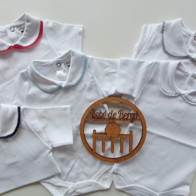 Cinco bodies brancos para bebés com golas de cores diferentes e placa de madeira com texto
