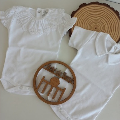 Dois bodies de bebé brancos com diferentes golas e botões de pressão, sobre superfície branca com decoração em madeira