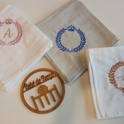 Três panos de prato bordados com letras e coroa, junto a enfeite de madeira