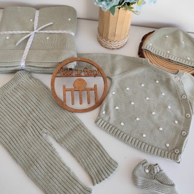 Conjunto de roupa de bebé tricotada em verde-acinzentado com pontos brancos sobre uma superfície branca