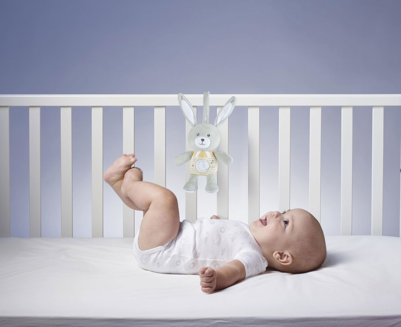 Bebé deitado num berço branco com brinquedo de coelho cinzento