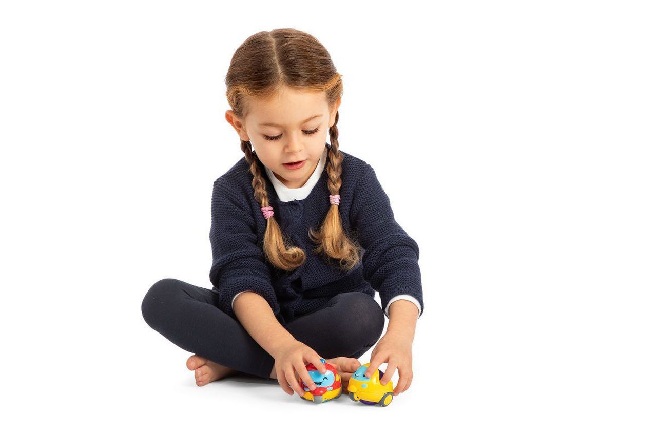 Menina com camisola azul escuro a brincar com carrinhos coloridos sentada no chão branco