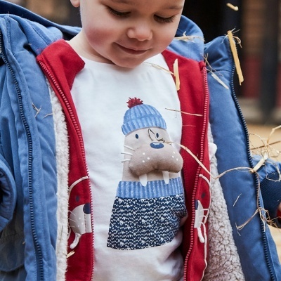 Criança com casaco azul e t-shirt branca com estampa de morsa com gorro azul