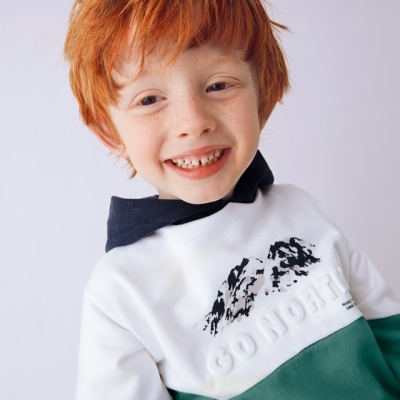 Criança ruiva com casaco verde e branco com estampa e texto GO NORTH