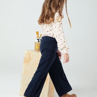 Criança com roupa casual em fundo neutro, vestindo botas castanhas com flores bordadas