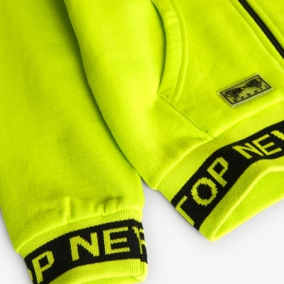 Detalhe de casaco amarelo neón com punhos elásticos e etiqueta junto ao bolso