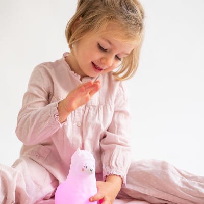 Menina com pijama rosa claro brincando com luz de lhama cor-de-rosa