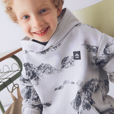 Criança com hoodie branco com padrão de montanhas sentado numa cadeira verde