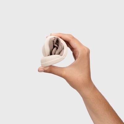 Mão segurando tecido enrolado bege sobre fundo cinza claro