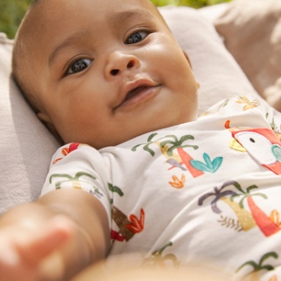 Bebé de body estampado deitado sobre almofada bege em ambiente exterior