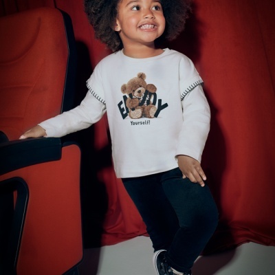 Criança de roupa casual com estampa de ursinho, em fundo vermelho com assento.