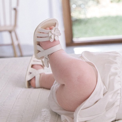 Sandálias brancas de bebé com flores decorativas usadas por bebé em tecido branco