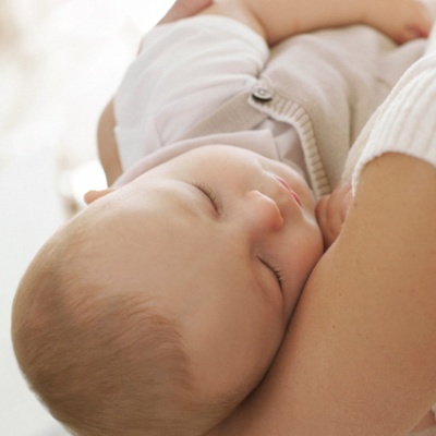 Bebé adormecido vestido de branco e bege a ser segurado por adulto