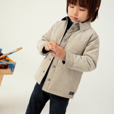 Criança a usar casaco bege com botões, junto a mesa com pincéis