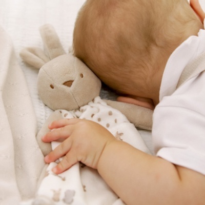 Bebé deitado a abraçar brinquedo de pelúcia coelho cinzento